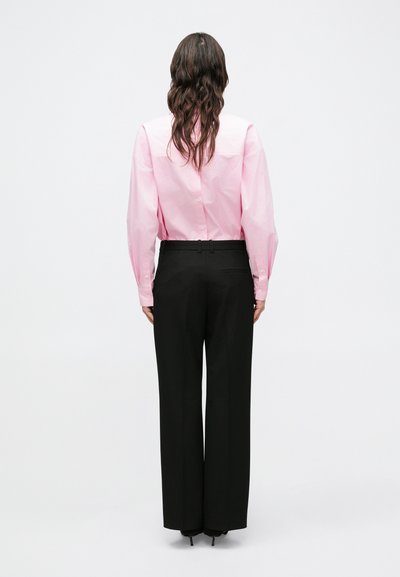 Svetloružová košeľa na gombíky s dlhými rukávmi, skombinovaná s čiernymi širokými nohavicami s vysokým pásom. Hladká textúra a priliehavý strih.