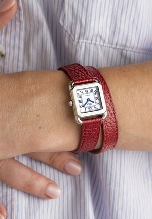 Zapestje z vitkim srebrnim kvadratnim uro z rimskimi številkami in modrimi kazalci, pritrjeno z teksturiranim rdečim usnjenim trakom za dvojno ovijanje.