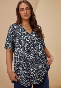 Marineblauw blouse met wit abstract patroon, V-hals, korte mouwen, losse fit en zachte textuur. Gestyled met donkere jeans.
