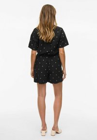 Romper nero a fantasia con maniche corte, vita elastica e disegni a diamante. Indossato con sandali con tacco a blocco di colore chiaro.