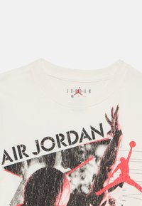 Λευκό βαμβακερό t-shirt με μαύρο και κόκκινο γραφικό τύπωμα και το κείμενο "AIR JORDAN", που απεικονίζει έναν παίκτη μπάσκετ σε δράση.