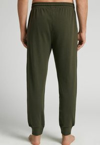Olijfgroene sweatpants met een elastische tailleband en taps toelopende boorden. Zachte stoftextuur met een relaxte pasvorm, gezien van achteren.