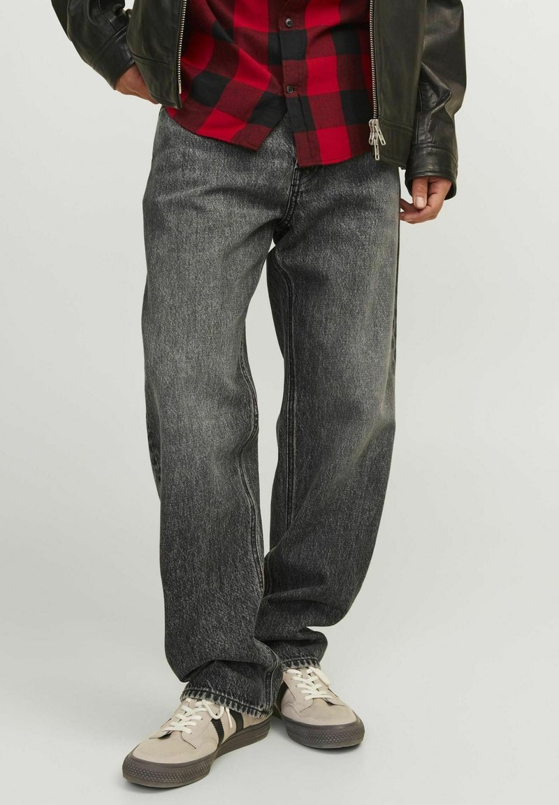 Vaqueros de mezclilla gris oscuro con un corte holgado, que presentan un ligero desgaste, bolsillos funcionales y se combinan con zapatillas beige y una camisa de cuadros roja.