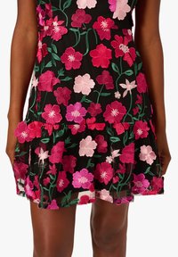 Krátké černé šaty s barevným květinovým vyšíváním v růžové a červené, s vrstveným volánkovým lemem a zelenými lístkovými akcenty.