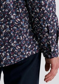 Langsleeve shirt in marineblauw met een bloemenpatroon in kastanjebruin, wit en blauw. Voorzien van een knoopsluiting bij de manchetten en een gebogen zoom. Gemaakt van katoen.
