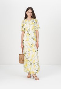 Rochie maxi florală albă cu grafică de lămâie galbenă, cu mâneci scurte puf încrețite, având o talie strânsă. Accesorizată cu o geantă din rafie.