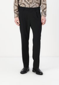Zwarte op maat gemaakte broeken met een platte voorkant, slim fit en subtiele textuur. Draagt een gestreepte longsleeve shirt en zwarte schoenen.