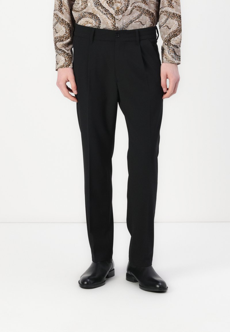 Zwarte op maat gemaakte broeken met een platte voorkant, slim fit en subtiele textuur. Draagt een gestreepte longsleeve shirt en zwarte schoenen.