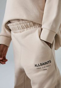 Beige Baumwoll-Sweatshirt mit geripptem Saum und Bündchen. Verfügt über einen elastischen Bund und eine Seitentasche, mit dem in Schwarz aufgedruckten "ALLSAINTS"-Logo.