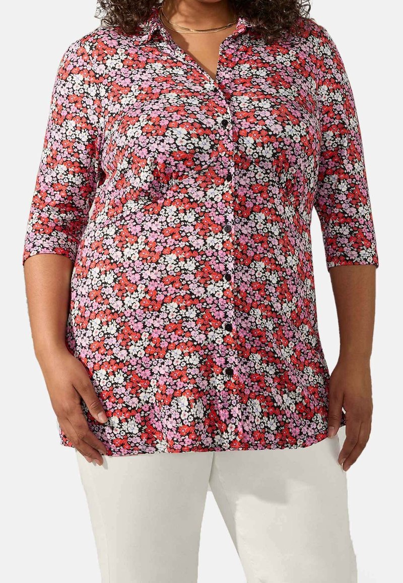 Camicia floreale bottone con sfondo nero e fiori rossi, rosa e bianchi, maniche a tre quarti e vestibilità leggermente ampia.
