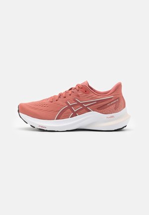 Zapatilla de correr color coral rosado con suela blanca, que cuenta con cuello acolchado, cordones y logo de Asics en el lateral, exhibida sobre un fondo blanco.