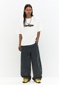 Hvid oversized t-shirt med et sort bilgrafik, parret med mørkeblå brede jeans med syede detaljer. Fodtøjet er gule sportsko.