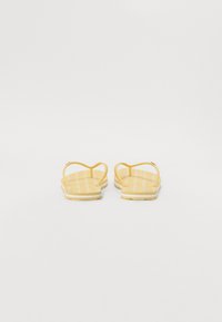 Tongs jaunes au design simple, avec des fines lanières et des semelles texturées. L'intérieur présente un texte en relief, indiquant la marque.