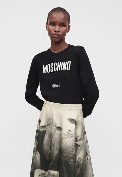 Personne portant un pull noir Moschino Milano et une jupe blanche avec un imprimé noir et blanc de moutons regroupés.
