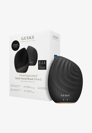 Brosse faciale en silicone noire avec une forme conviviale, un motif en vagues à l'avant et des accents dorés sur la base. Comprend un emballage élégant.