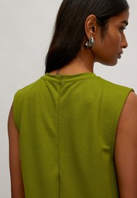 Grünes ärmelloses Top aus weichem Stoff, mit hohem Kragen, Reißverschlussverschluss auf der Rückseite und dezenter Textur.