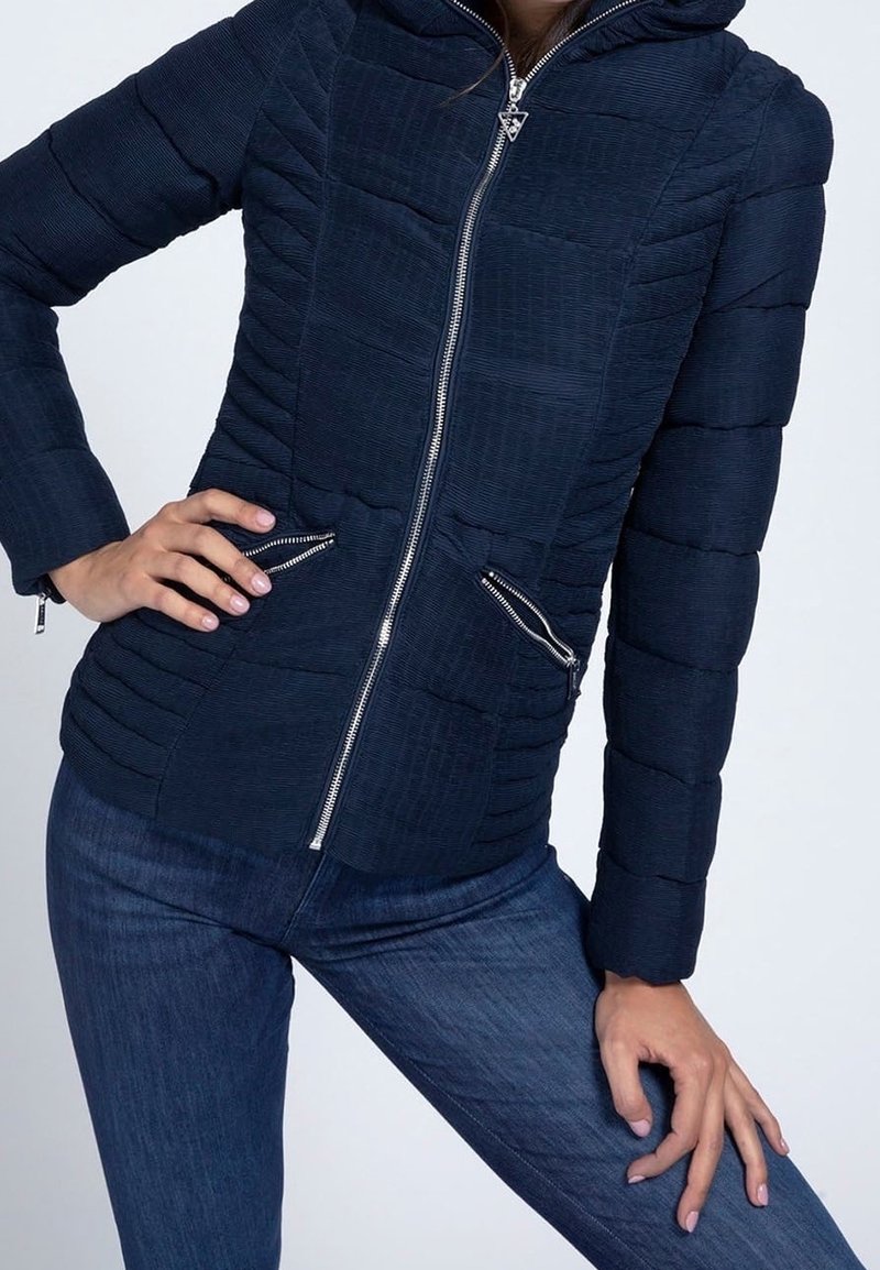 Námořnicky modrá péřová bunda s texturovaným povrchem, vybavená předním zipem, dvěma bočními kapsami a kapucí. Celý model má horizontální prošívání.