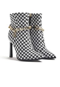 Černobílé houndstooth kotníkové boty s špičatou špičkou, vysokým jehlovým podpatkem, zipovým uzávěrem a zlatým řetízkovým akcentem.