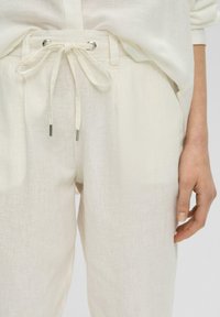 Lnianowe spodnie w odcieniu ecru o luźnym kroju, z elastycznym paskiem w talii, srebrnymi akcentami oraz bocznymi kieszeniami. Gładka tekstura.