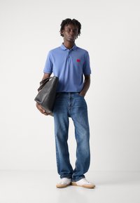 Lyseblå polo skjorte med en rød logo, parret med løse blå jeans, hvite joggesko og en svart toteveske. Glatt stoff og uformell passform.