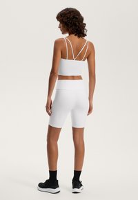 White athletic crop top with multiple thin straps at the back, paired with high-waisted white shorts. Worn with black athletic shoes and socks.