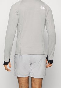 Camisa de manga larga gris claro con detalles en negro, que presenta un cuello redondo y agujeros para los pulgares, combinada con pantalones cortos gris claro.