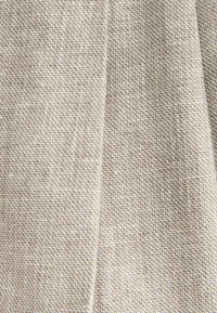 Tessuto intrecciato beige e bianco con un motivo a zigzag a piccola scala ripetuto e una cucitura verticale centrale.