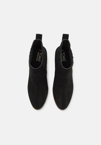 Botas de tobillo de ante negro con una textura suave, punta redondeada y paneles laterales elásticos para facilitar su puesta. Logo visible en la plantilla.