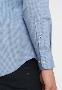  Lichtblauw button-up shirt met een ruitpatroon, voorzien van witte knopen en een getailleerde pasvorm, te zien op een donkere broek.