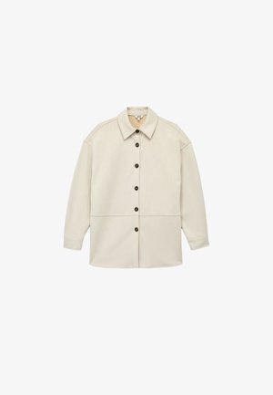 Veste chemise beige à boutons, fabriquée en tissu doux, avec un col évasé, des manches longues et deux coutures horizontales sur le corps.