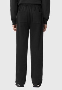 Czarne dresy o luźnym kroju, z elastycznym pasem i dwoma tylnymi kieszeniami. Wykonane z miękkiego materiału, charakteryzują się gładką teksturą i prostymi nogawkami.