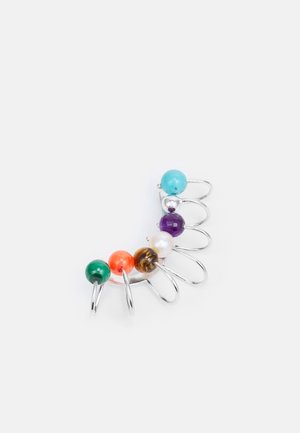 Anillo de alambre de plata con siete cuentas de colores: verde, naranja, marrón, blanco, morado, plata y turquesa, dispuestas en una línea curva.