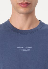 Navy blue cotton crewneck t-shirt with ribbed neckline and white text: "SAMSØE SAMSØE COPENHAGEN" centered on the chest.