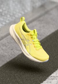 Chaussure de sport jaune vif avec une tige texturée, des accents réfléchissants et une semelle rembourrée. Conçue pour le confort léger et la performance.