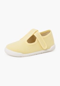 Chaussure en toile jaune avec une bande Velcro et un design découpé, dotée d'une semelle en caoutchouc blanche et d'un dessus texturé pour une meilleure adhérence.