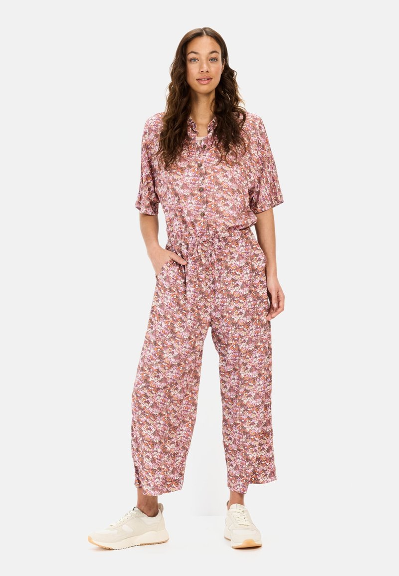 Bloemenoverall in roze tinten met korte mouwen, knoopsluiting aan de voorkant, elastische taille en brede cropped benen, gecombineerd met lichte sneakers.