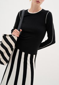 Melnas garām piedurknēm tops ar baltu apmalīti, saskaņots ar melnbaltu svītrainu svārku. Somiņa ir ar uzsvērtām horizontālām svītrām.