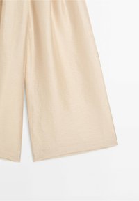 Pantalon beige à jambes larges en tissu lisse, légèrement brillant, avec une coupe décontractée, présenté sur fond blanc.
