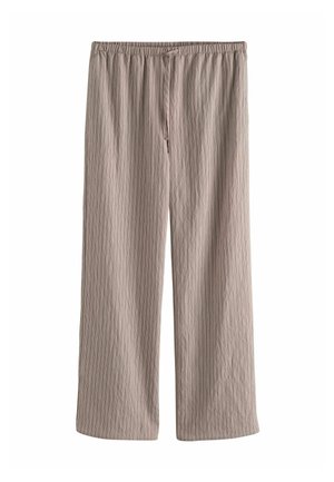 Personne portant un pantalon et un haut à rayures marron, ajustant l'ourlet avec la main droite montrant des bagues sur deux doigts.