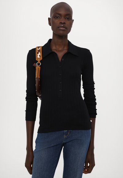 Svart ribbet langermet polo skjorte med knappelukking foran, spiss krage og teksturert stoff, kombinert med blå denimjeans.
