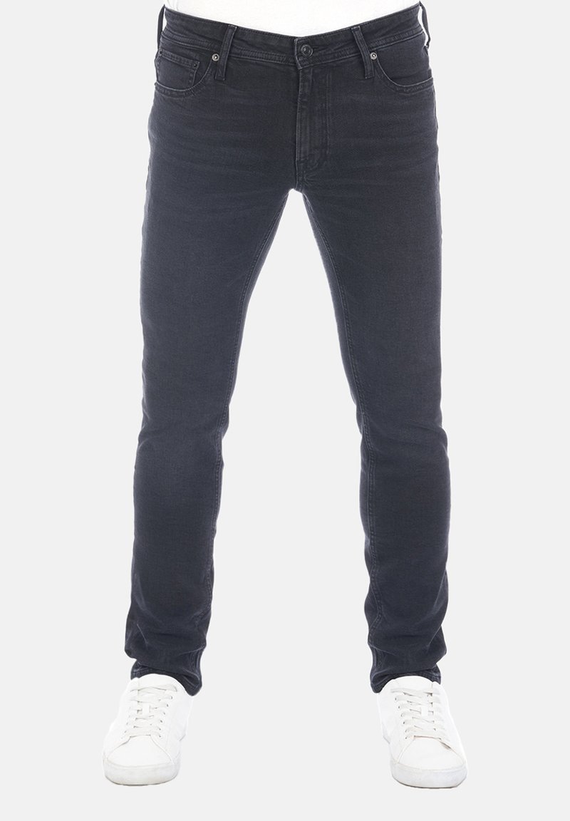 Jeans de mezclilla negros con un corte ajustado, diseño de cinco bolsillos y detalles de costura sutiles, combinados con zapatillas blancas sobre un fondo claro.