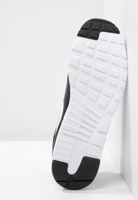 Svart och vit atletisk skosula med texturmönster i gummi. Har formar med spår och "Nike"-logotypen nära hälen.