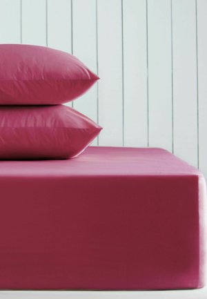 Due cuscini rosa impilati su un letto con lenzuolo aderente rosa abbinato contro una parete bianca con pannelli verticali.