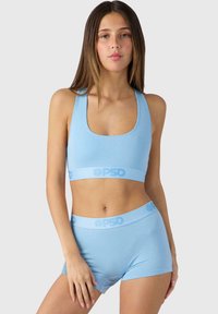 Šviesiai mėlynas sportinis liemenukas ir šortai, pagaminti iš švelnios medžiagos, su logo juosta juosmens srityje ir apvaliu iškirpimu liemenuko priekyje.