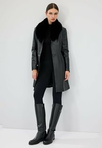 Czarna skórzana kurtka z kołnierzem z sztucznego futra, z zapięciem na guziki i eleganckim krojem. W połączeniu z czarnymi legginsami i skórzanymi botkami do kolan.