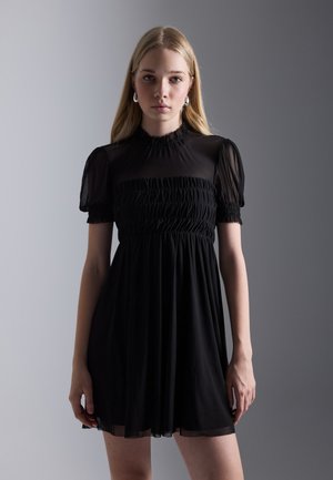Schwarzes Kleid mit durchsichtigen kurzen Puffärmeln und gerafftem Oberteil. Fließender Rock mit weicher Textur, hochgeschlossen und knielang geschnitten.