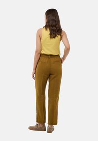 Haut sans manches jaune associé à un pantalon moutarde taille haute et fuselé. Le pantalon présente un tissu texturé et des poches arrière. Chaussures décontractées.