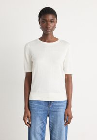 Haut en tricot blanc à manches courtes avec un col rond et un ourlet côtelé, associé à un jean droit bleu clair. Texture lisse, design minimal.