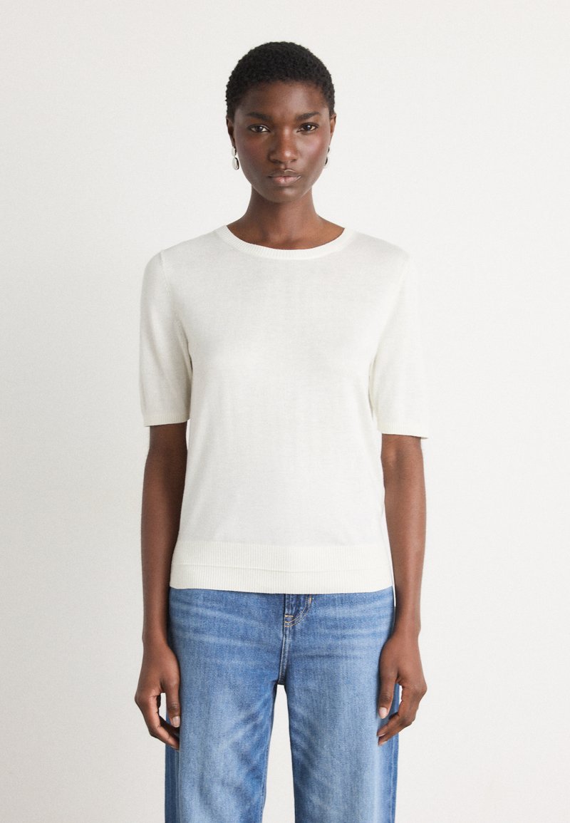 Haut en tricot blanc à manches courtes avec un col rond et un ourlet côtelé, associé à un jean droit bleu clair. Texture lisse, design minimal.