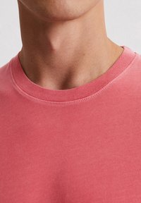 Light pink crew neck sweatshirt featuring a smooth texture and stitching detail on the collar. Close-up view focusing on the neckline.